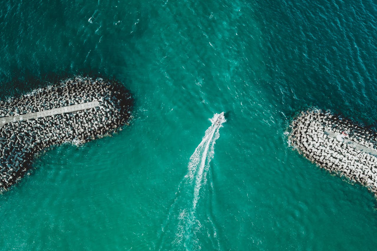 Drone captures a boat speeding through turquoise waters between rocky jetties.